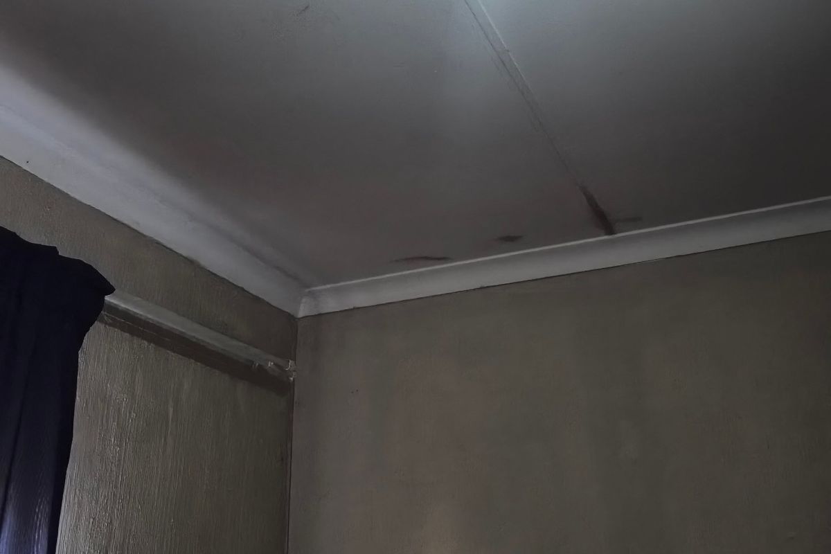 A bedroom interior showing visible water damage and cracking on the ceiling surface, requiring maintenance and repair.