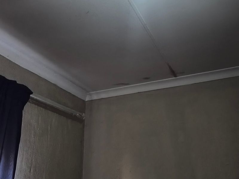 A bedroom interior showing visible water damage and cracking on the ceiling surface, requiring maintenance and repair.