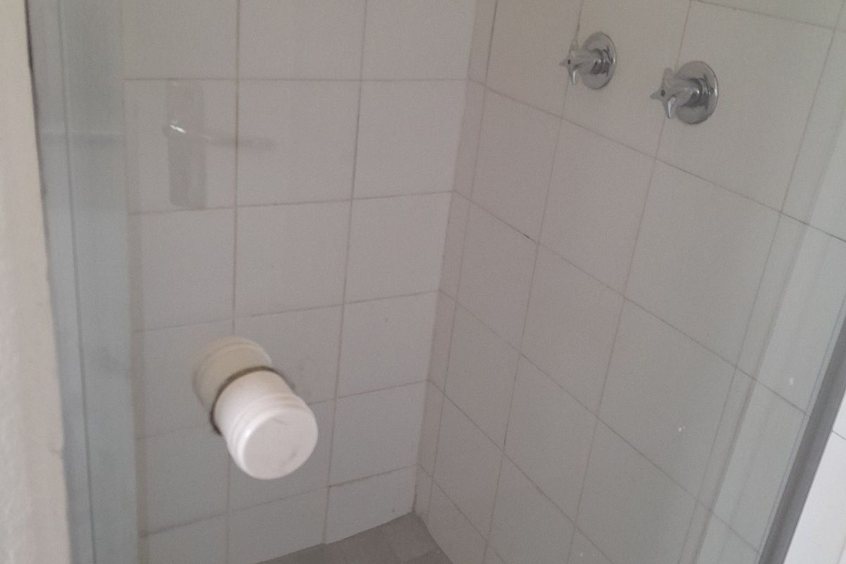 A basic shower stall featuring white wall tiles and chrome mixer taps, currently missing a shower head fixture.