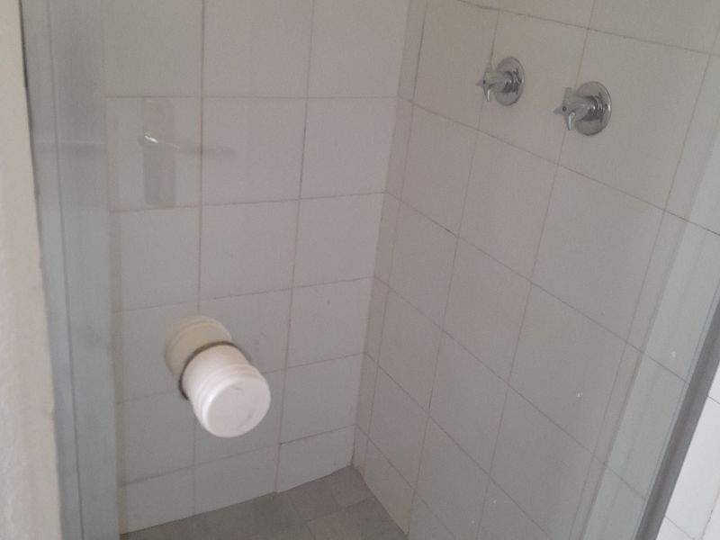 A basic shower stall featuring white wall tiles and chrome mixer taps, currently missing a shower head fixture.