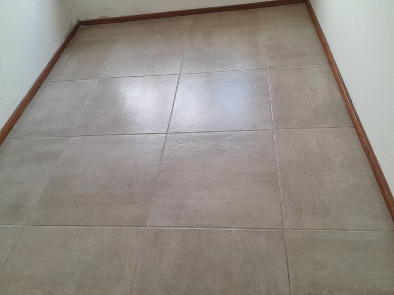 An empty room featuring neutral ceramic floor tiles and timber skirting boards, presenting a clean canvas for interior design.