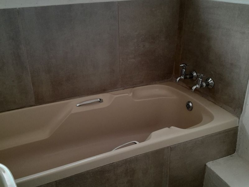 A functional bathroom featuring a built-in bathtub with chrome fixtures and neutral wall tiling.