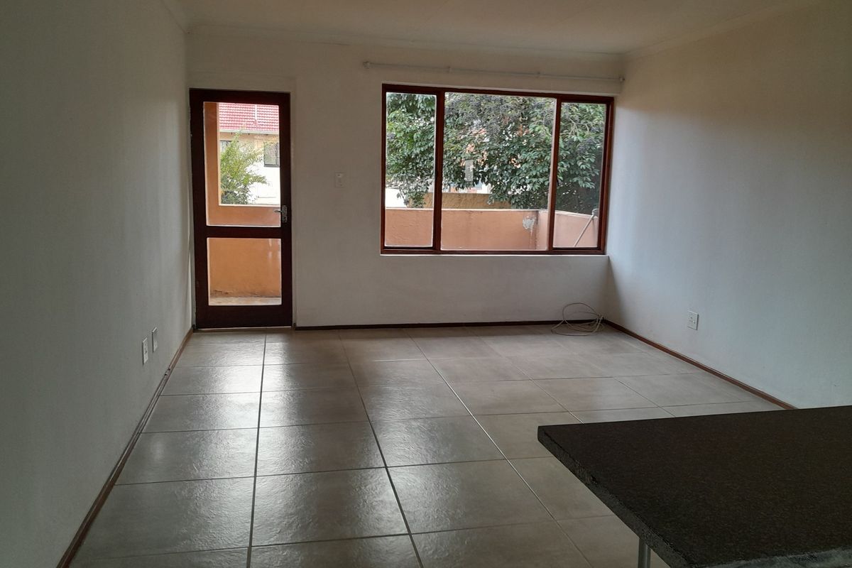 An empty, open-plan living area featuring neutral tiled flooring, a breakfast bar, and natural light through a large window and glass door.