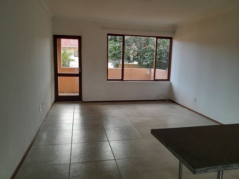 An empty, open-plan living area featuring neutral tiled flooring, a breakfast bar, and natural light through a large window and glass door.