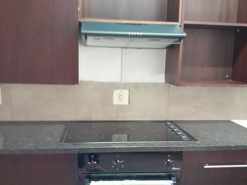 A kitchen area featuring dark wood cabinetry, granite countertops, a built-in oven, and an electric hob with an extractor fan.