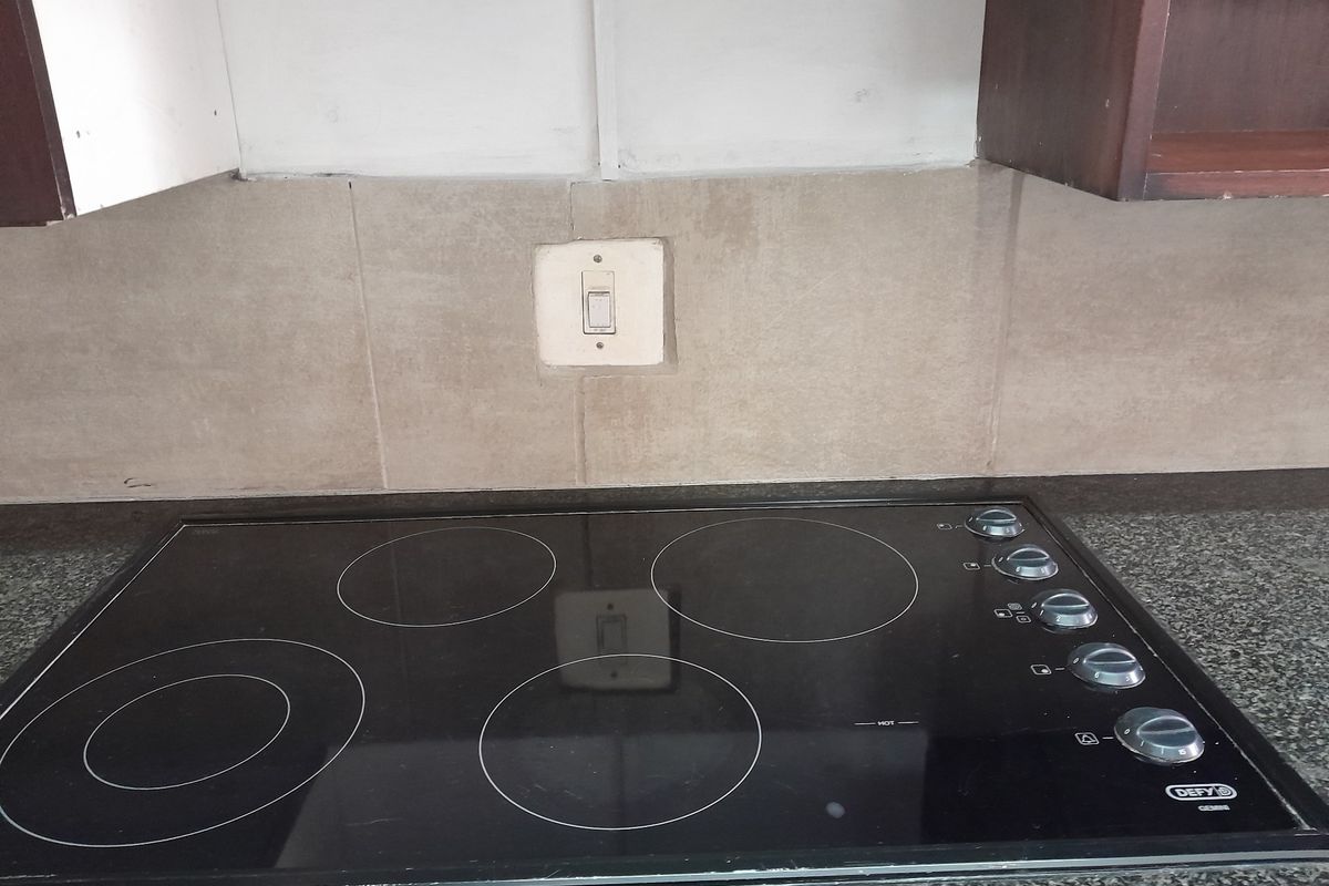 A close-up view of a kitchen workspace featuring a black electric hob set into a granite countertop with a tiled backsplash and upper cabinetry.