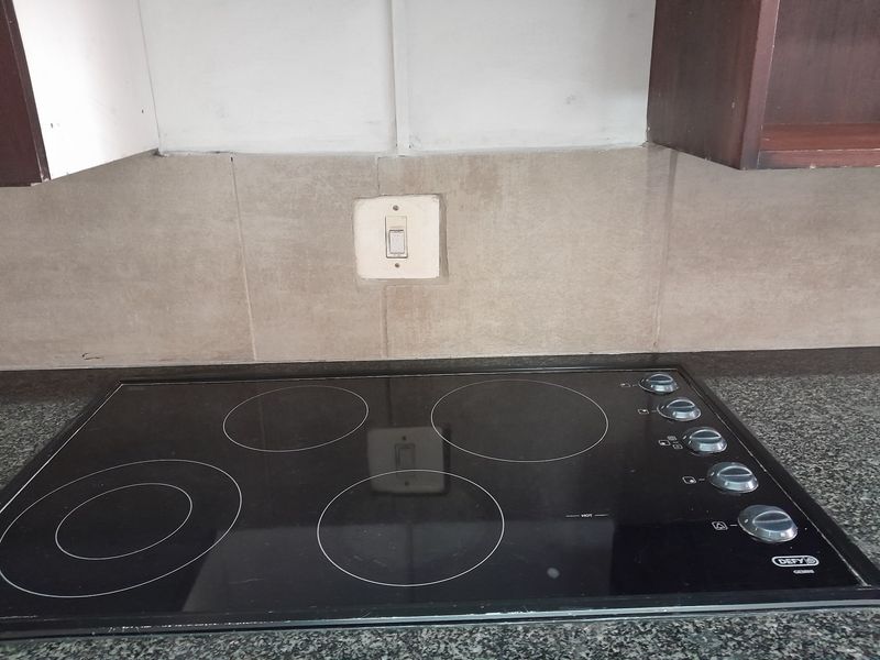 A close-up view of a kitchen workspace featuring a black electric hob set into a granite countertop with a tiled backsplash and upper cabinetry.