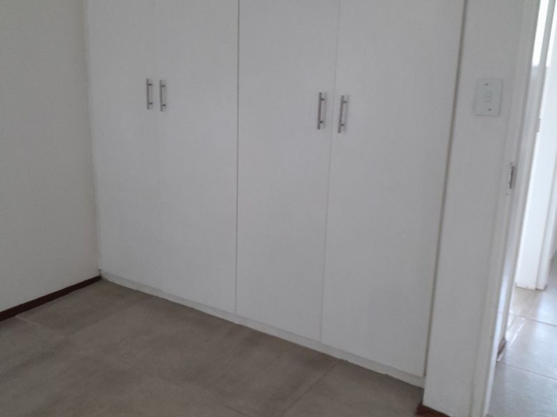 A clean, empty bedroom featuring neutral tiled flooring and white built-in cupboards, offering a versatile space ready for personalization.