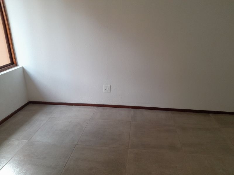 An empty bedroom featuring neutral tiled flooring, dark timber skirting boards, and a single electrical outlet on a plain wall.