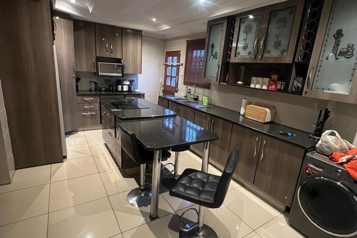 Modern kitchen featuring dark wood cabinetry, granite countertops, a central island with breakfast bar, and large format ceramic floor tiles.