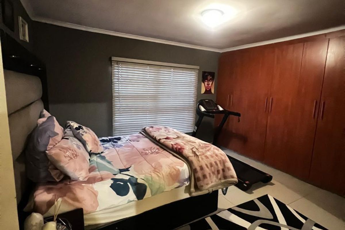 A bedroom featuring built-in wooden cupboards, tiled flooring, and venetian blinds, providing a functional space with ample storage.