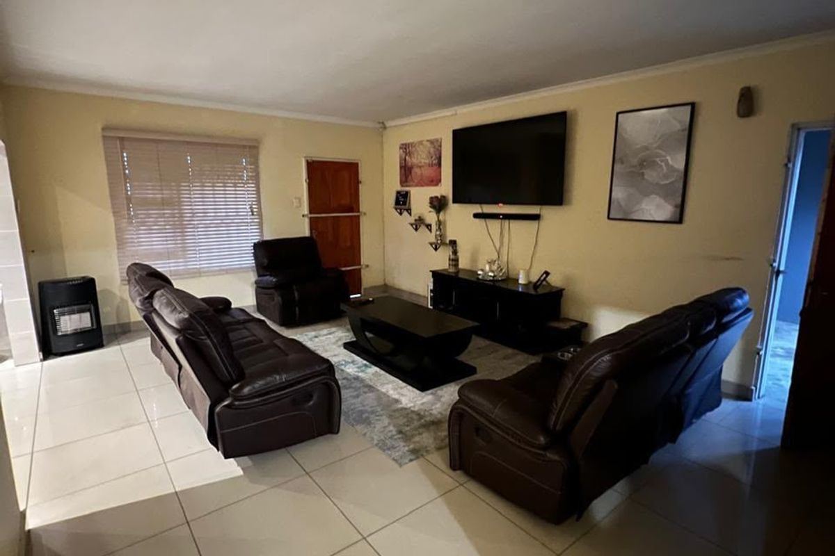 A living room featuring tiled flooring, venetian blinds, and a wall-mounted gas heater, providing a functional and comfortable space.