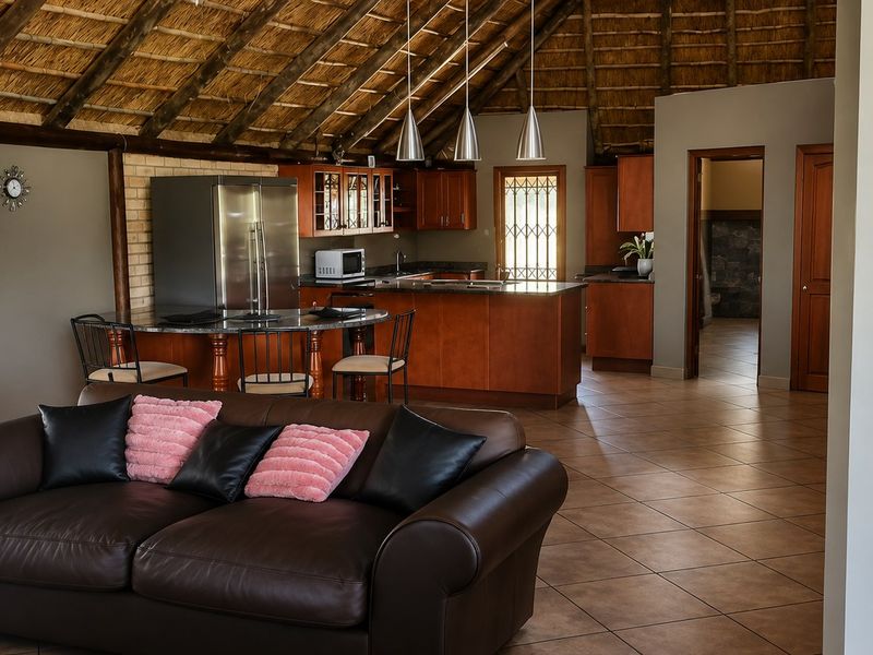 Spacious open-plan living and kitchen area featuring a traditional thatched roof with exposed timber rafters, tiled floors, and a functional kitchen with granite countertops.