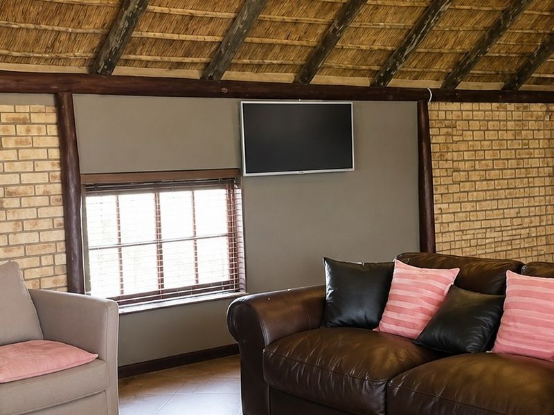 A cozy living room featuring a high vaulted thatched ceiling with exposed timber rafters, exposed brick walls, and a classic wrought iron chandelier.
