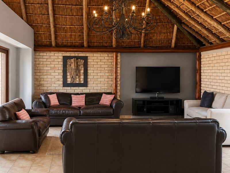 Spacious living room featuring a high vaulted thatch ceiling with exposed timber rafters, exposed brick walls, and a classic wrought iron chandelier.
