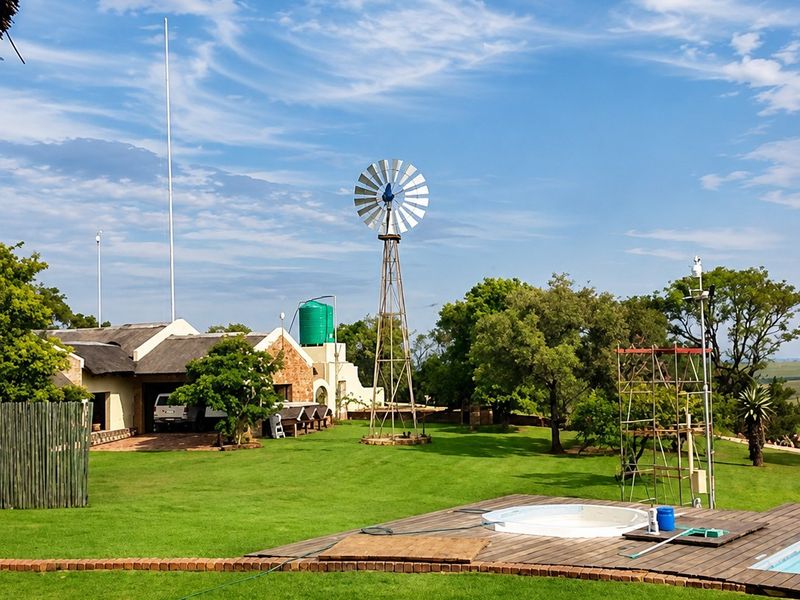 Expansive farm garden featuring a traditional windmill, water storage tank, and a wooden deck surrounding a swimming pool with views of the property.