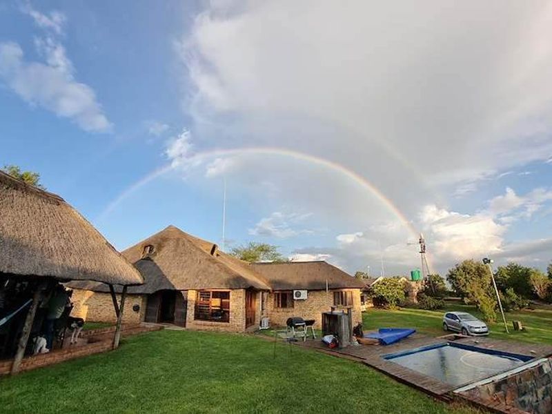 Rear view of a farm-style property featuring a thatched roof, brick exterior, swimming pool, and a windmill set against a scenic landscape.