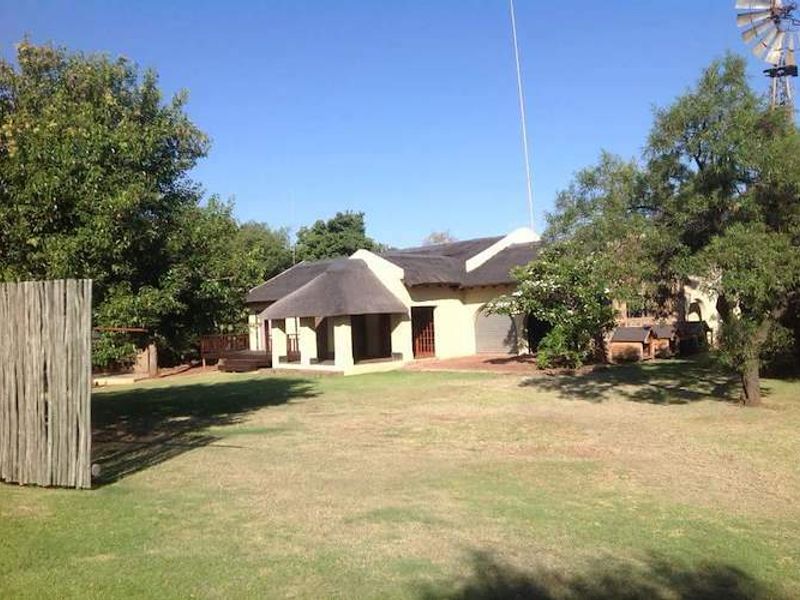 Rear view of a farm-style dwelling featuring a traditional thatch roof, a covered patio area, and a classic windmill set within a spacious garden.