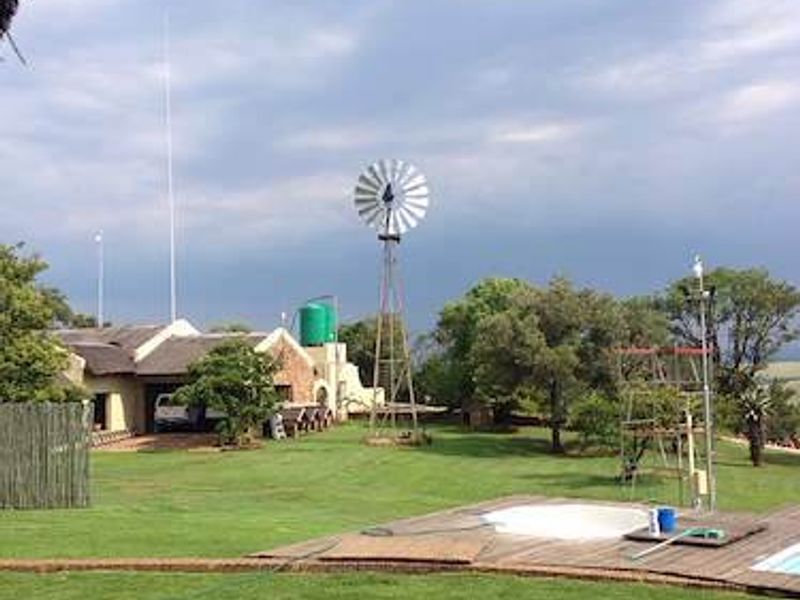 Spacious farm garden featuring a traditional windmill, water tank, thatched roof dwelling, and a swimming pool with wooden decking.