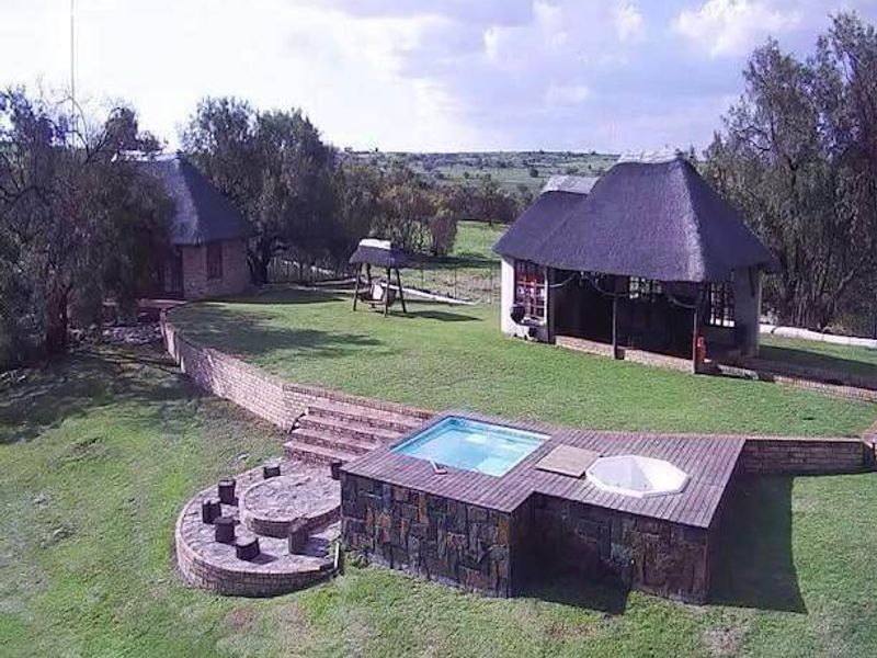 Aerial view of a farm property featuring thatched roof buildings, a swimming pool, a hot tub, timber decking, and a stone fire pit area.