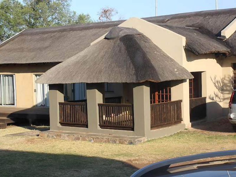 Rear view of a farm-style dwelling featuring a covered patio with a traditional thatch roof, timber balustrades, and wooden decking.