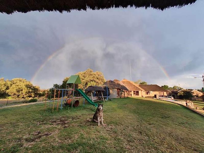 A wide-angle view of the rear garden and farm dwelling featuring traditional thatch roofing under a rainbow.