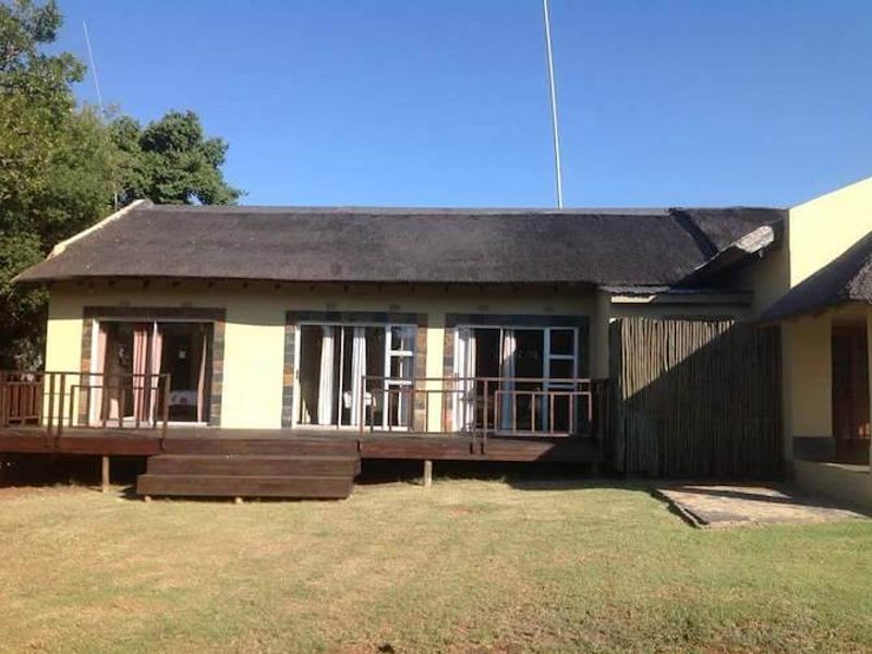 Rear view of a farm-style dwelling featuring a thatched roof, a raised timber deck, and multiple sliding glass door access points.