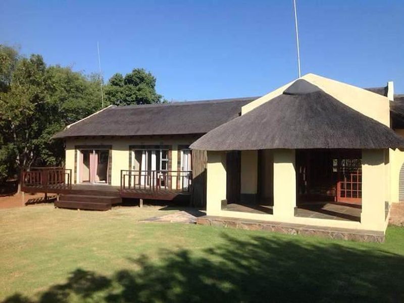 Rear view of a farm-style residence featuring a thatched roof, a raised timber deck, and a covered patio area overlooking the garden.
