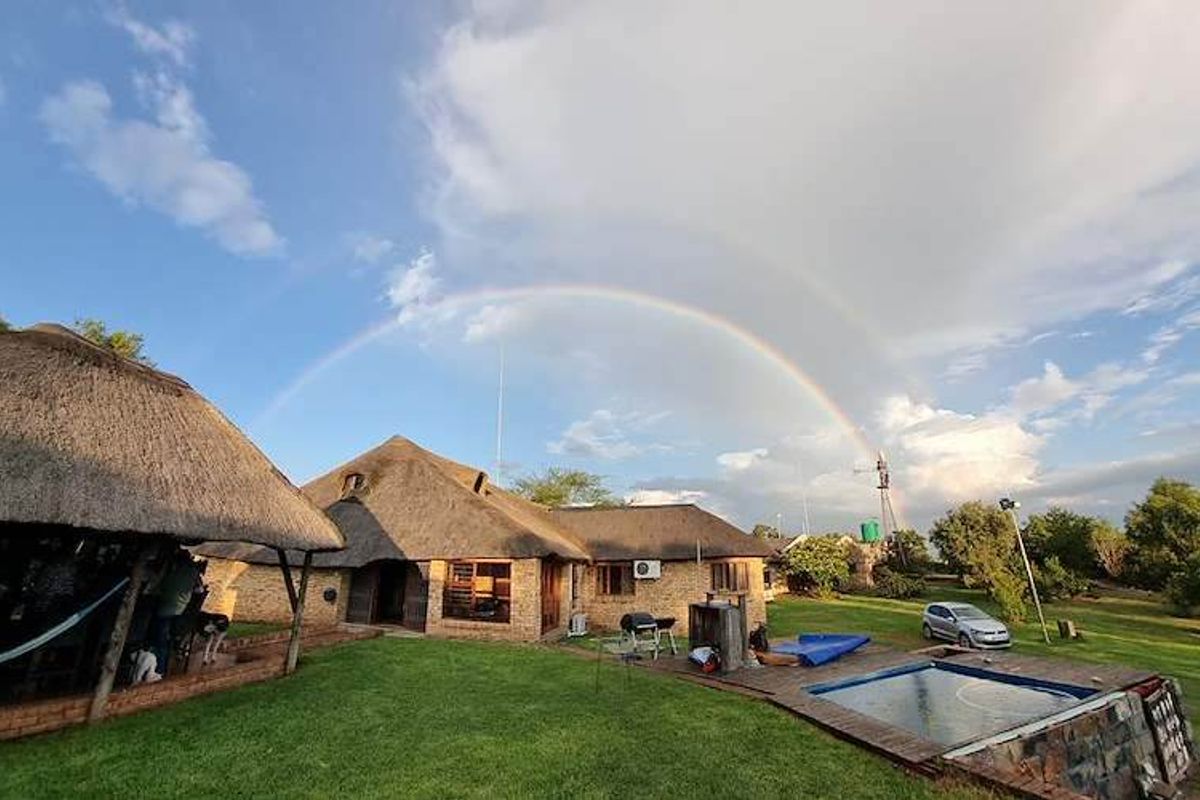 Rear view of a farm-style property featuring a thatched roof, brick exterior, swimming pool, and a windmill set against a scenic landscape.