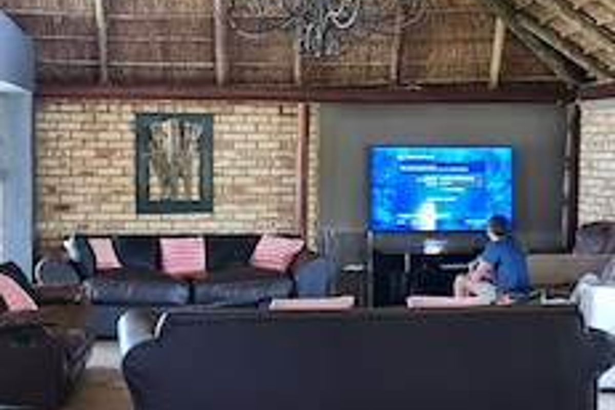 Spacious living area featuring a high vaulted thatched roof with exposed timber rafters, exposed brick feature wall, and ceramic tiled flooring.