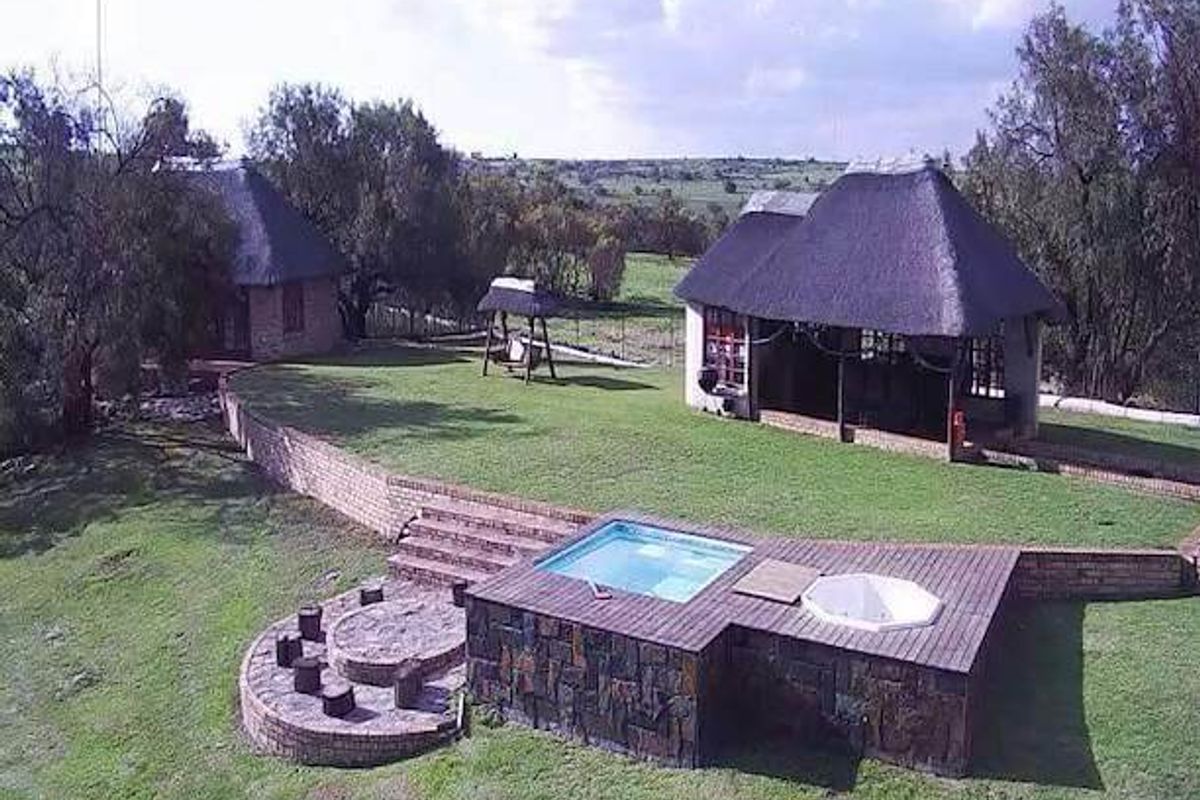 Aerial view of a farm property featuring thatched roof buildings, a swimming pool, a hot tub, timber decking, and a stone fire pit area.