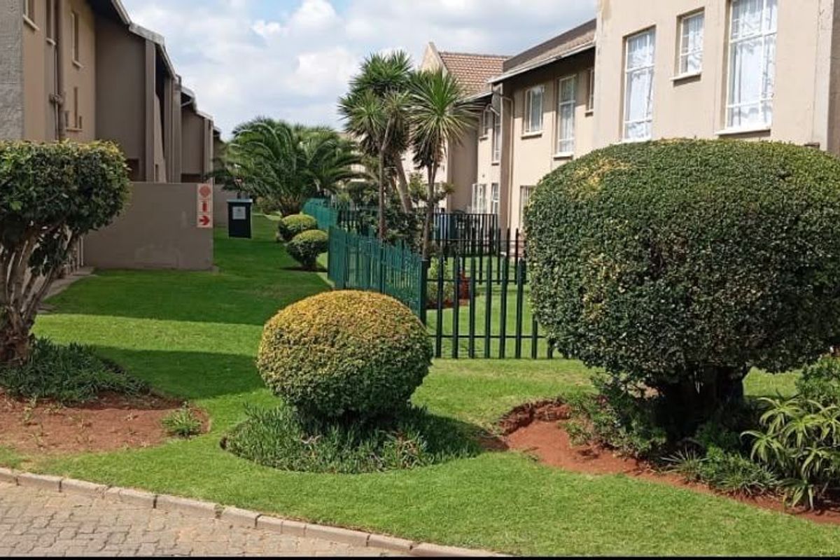 A view of the communal garden area and apartment building exterior, featuring well-maintained landscaping and paved pathways between residential units.