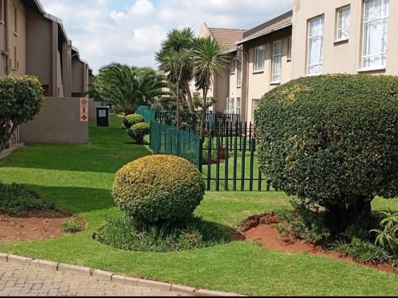 A view of the communal garden area and apartment building exterior, featuring well-maintained landscaping and paved pathways between residential units.