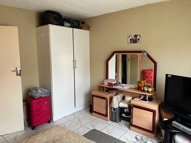 A bedroom featuring tiled flooring and a built-in wardrobe, currently showing signs of wear on the ceiling and floor tiles.
