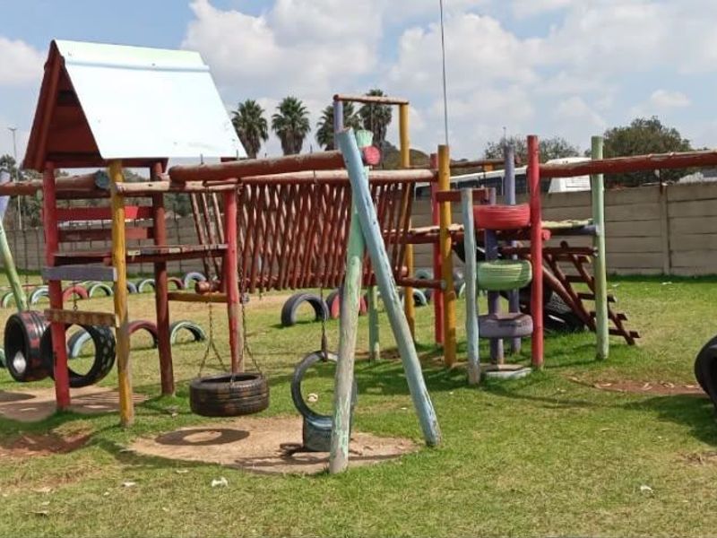 Outdoor communal playground area featuring various timber climbing structures and tire-based play equipment within a fenced complex.