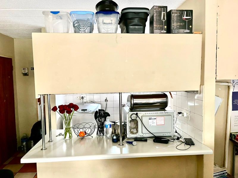A kitchen service counter area featuring a tiled backsplash, laminate countertop, and overhead cabinetry, showing signs of wear and dated finishes.