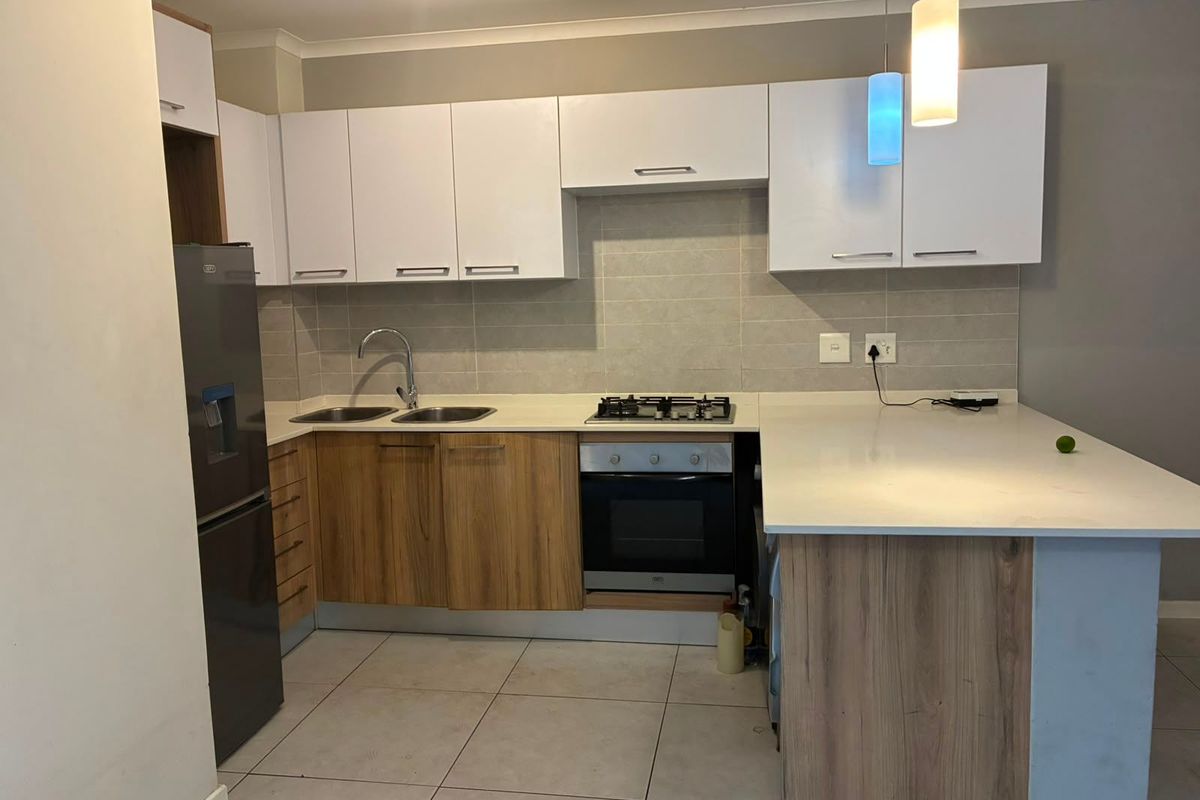 Modern kitchen featuring two-tone cabinetry, stone countertops, integrated gas hob, built-in oven, and tiled backsplash with functional breakfast bar area.