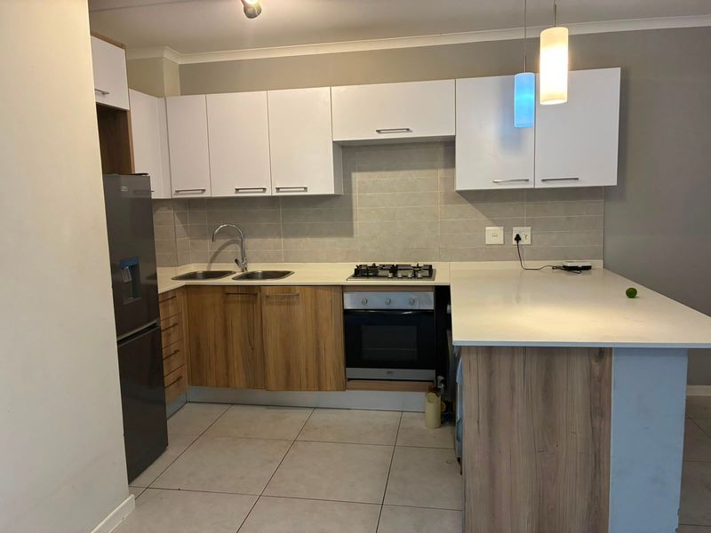 Modern kitchen featuring two-tone cabinetry, stone countertops, integrated gas hob, built-in oven, and tiled backsplash with functional breakfast bar area.