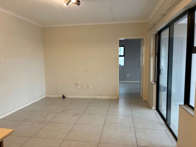 An empty living room featuring neutral tiled flooring, a sliding glass door providing natural light, and access to an adjacent room.