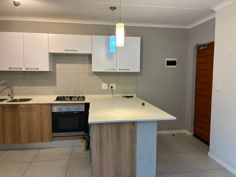 Modern kitchen featuring white and wood-grain cabinetry, stone countertops, a gas hob, built-in oven, and tiled backsplash with contemporary pendant lighting.