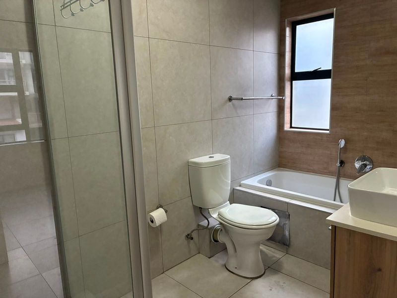 Modern bathroom featuring a shower enclosure, bathtub, vessel sink with vanity, and neutral floor-to-ceiling tiling.