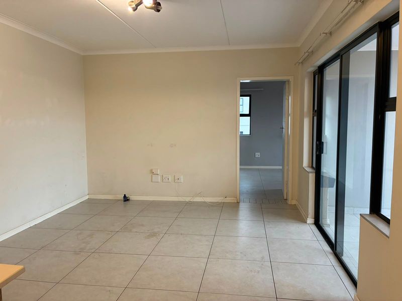 An empty living room featuring neutral tiled flooring, sliding glass doors providing natural light, and access to an adjacent room.