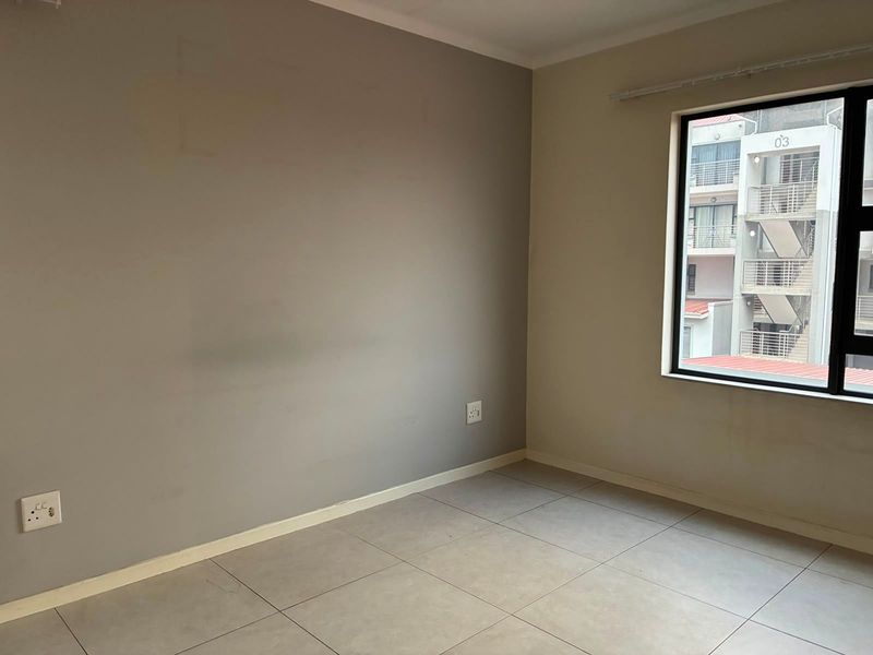 An empty bedroom featuring neutral tiled flooring, grey accent wall, and an aluminium-framed window with views of the adjacent building.