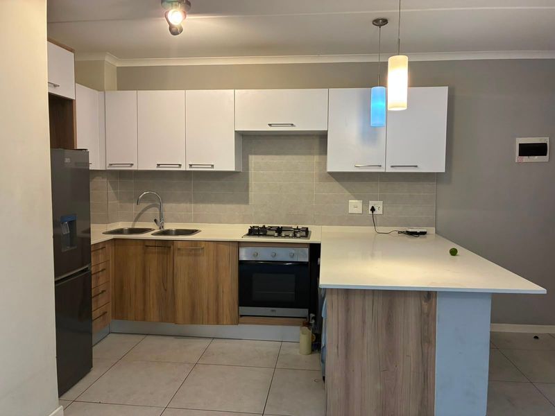 Modern kitchen featuring wood-grain and white cabinetry, stone countertops, integrated gas hob, built-in oven, and stylish pendant lighting.