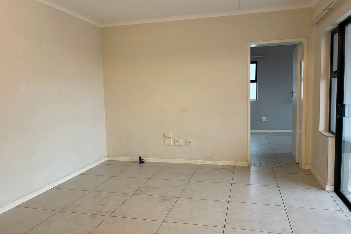 An empty, neutral-toned living area featuring tiled flooring, coved ceilings, and a sliding glass door leading to an outdoor space.