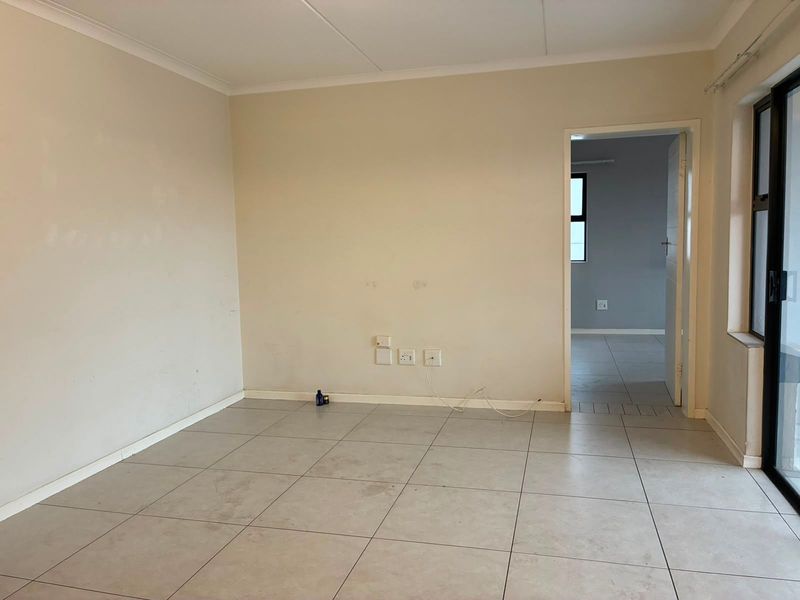 An empty, neutral-toned living area featuring tiled flooring, coved ceilings, and a sliding glass door leading to an outdoor space.