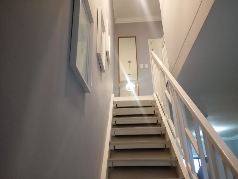 A bright staircase with a white wooden balustrade leading to an upper landing, featuring neutral wall tones and clean architectural lines.