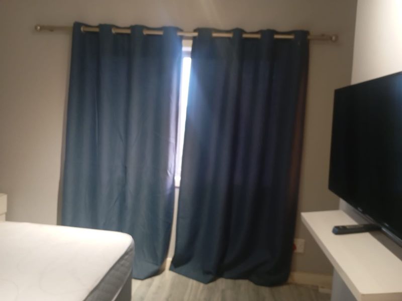 A bedroom featuring a floating shelf and window with curtain rod, finished with light-toned flooring.