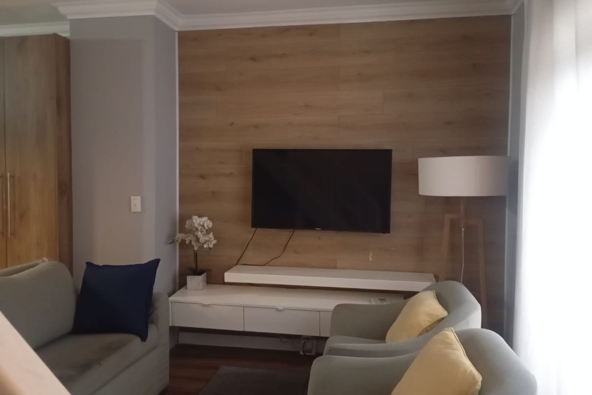A cozy living room featuring a wood-paneled accent wall with a mounted television and a sleek, white floating media console.