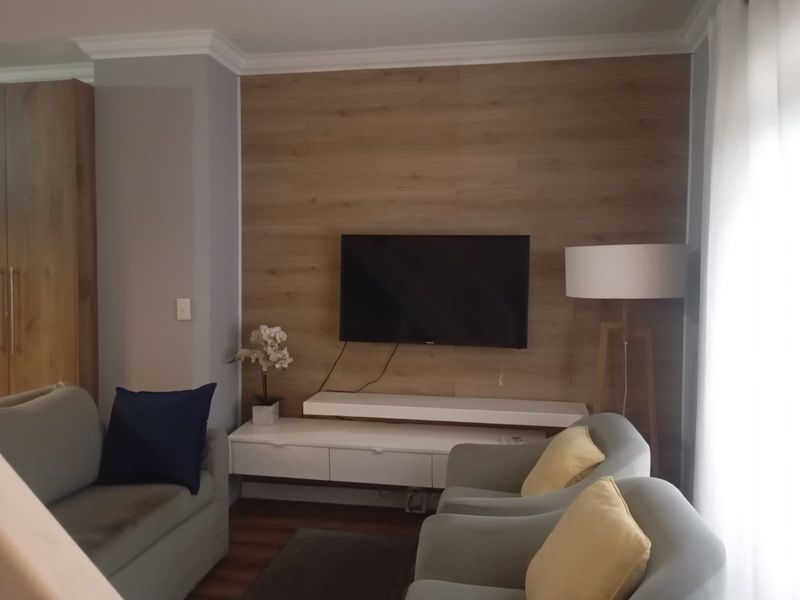 A cozy living room featuring a wood-paneled accent wall with a mounted television and a sleek, white floating media console.